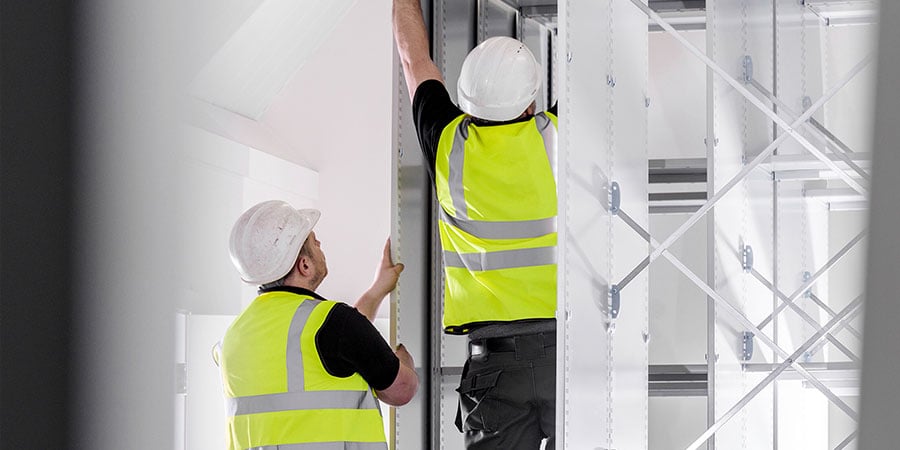 Two construction workers installing containment panels in a healthcare construction area to support construction dust control.