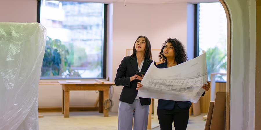 Two professionals reviewing construction plans inside a healthcare renovation space with exposed framing and temporary containment setup