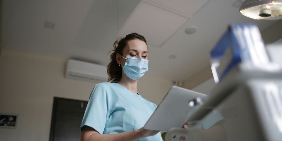 Masked clinician reviewing a tablet in an operating room, representing ASC teams evaluating portable HEPA filtration and air control without disrupting OR schedules.