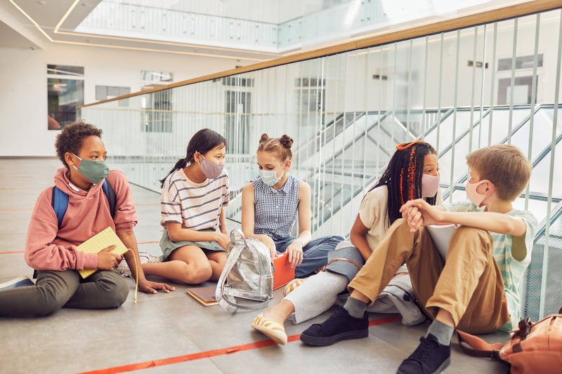 Group of children wearing masks, sitting outside the classroom. 