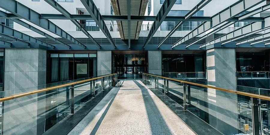Hospital breezeway corridor with glass walls and overhead structural framing, illustrating airflow pathways in an active healthcare environment