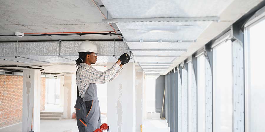 Construction worker installing overhead ductwork in an active renovation space, highlighting hospital construction conditions where dust containment and airflow control are critical