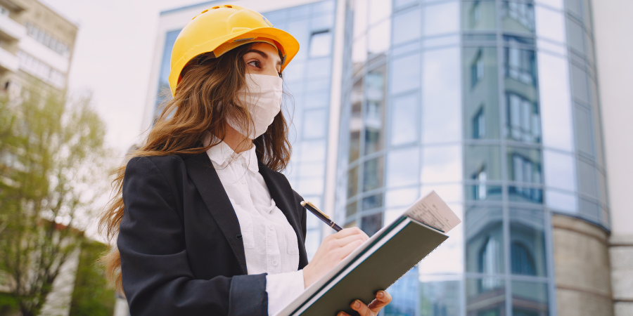 Woman writing on a clip board wearing a hard hat